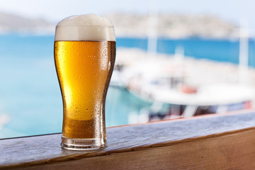 Glass of light beer on the  seaside bar counter.Boats in the doc