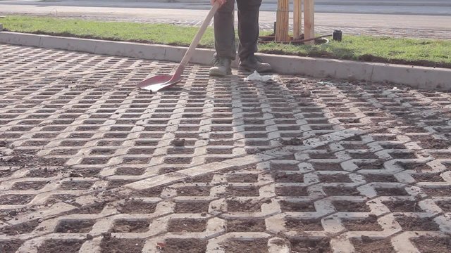 Dirt stripping, scraping with red shovel, cleaning urban ground. Worker is scraping the dry mud off new placed cobblestone with red shovel.
