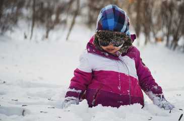 Fototapeta na wymiar Caucasian little girl in winter clothes playing in the snow