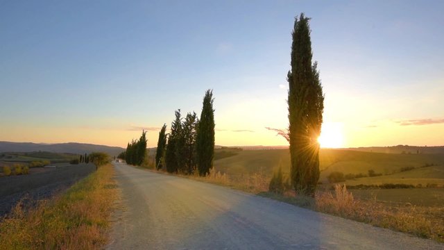 Fast moving car on the dirt road in Tuscany at sunset.