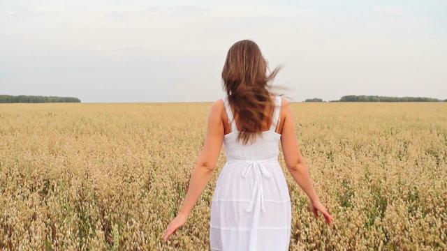 Rear view of woman in white dress running through the golden field of rye in slow motion