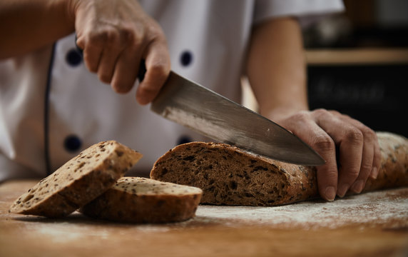 Woman chef cutting healthy bread with seeds on wooden board. Bakehouse. Bread production.