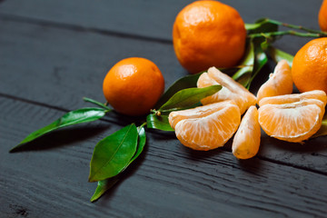 Beautiful ripe tangerines with leaves on a black wooden background