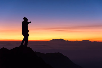 silhouette of man standing and thumbs up on the top of mountain
