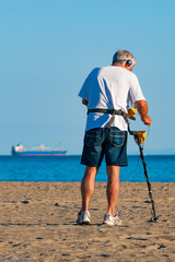 man uses metal detector on a beach