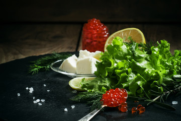 Red salmon caviar in a silver spoon on a black stone background