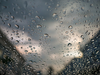Raindrops on car's glass with blurry cloudy sky and village in o