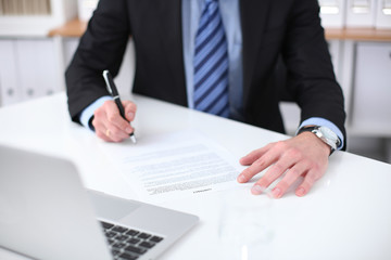 Young business man signs contract sitting at the desk in office