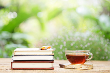 tea in glass and notebook with pens on wooden table at outside
