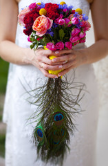 Свадебный букет из роз, гвоздик, васильков и павлиньих перьев в руках невесты в белом платье