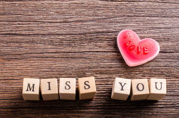 Heart shaped chewing candy and words "miss you" on cubes,  wooden background. Vintage effect. Free space for your text