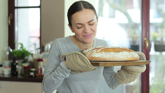 Young woman smelling freshly baked bread in kitchen