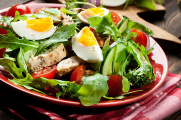 Fresh salad with chicken, tomatoes, eggs and arugula on plate