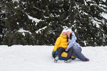 Fototapeta na wymiar Young happy couple walking in the park in winter. Beautiful lovers ride on a roller coaster tubing. A man and a woman go through the forest and hold each other's hands.