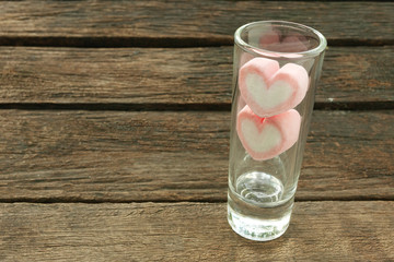 The lovely pink heart marshmallows in small narrow glass on old deep brown planks for Valentine's day.