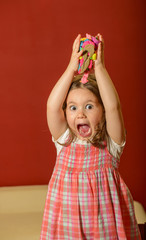 Expressive beautiful little girl playing indoor with colored pieces of clay, plasticine, being inventive 