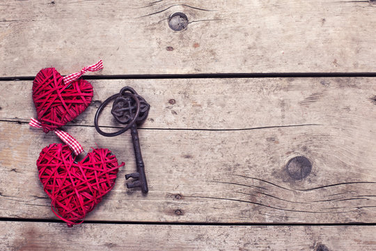 Two red decorative  hearts and key on vintage wooden background