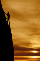 silhouette of a woman climbing a large steep mountain with a bac