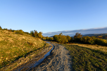 Fototapeta na wymiar Rural road in autumn landscape. Mountain rural road with water a