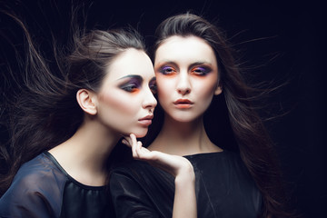Portrait of two beautiful young girls twins in the studio with bright makeup on a black background, the concept of beauty