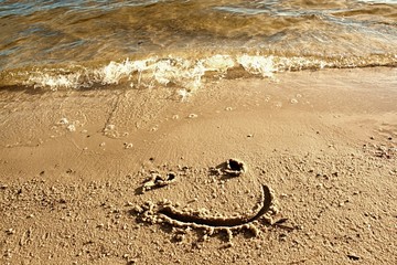 Funny smile face drawn on wet sand near sea