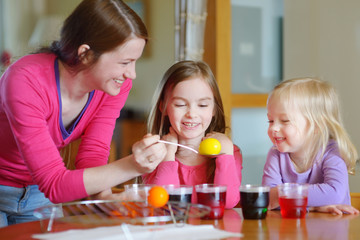 Young mother and her two daughters painting Easter eggs