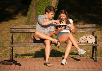 Young couple having fun on a bench in park while socializing ove