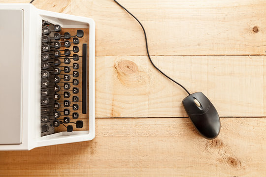 The image shows an antique typewriter connected to a computer mouse imitating a laptop and conceptualizing the obsolescence of technology 