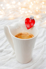White cup of hot coffee with decorative heart and engagement diamond ring,