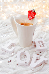 White cup of hot coffee with decorative heart and engagement diamond ring,
