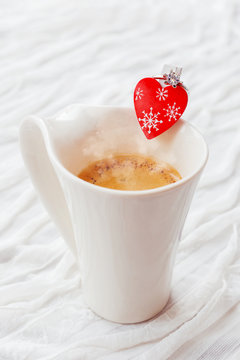 White cup of hot coffee with decorative heart and engagement diamond ring,