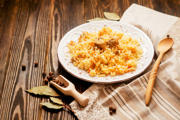 
national cuisine , stewed rice with meat , which is called pilaf with bay leaf and pepper on a wooden background 