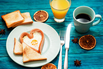 
romantic breakfast , heart-shaped fried eggs with sausage with toast, jam , hot black coffee , orange juice and spices on a wooden background