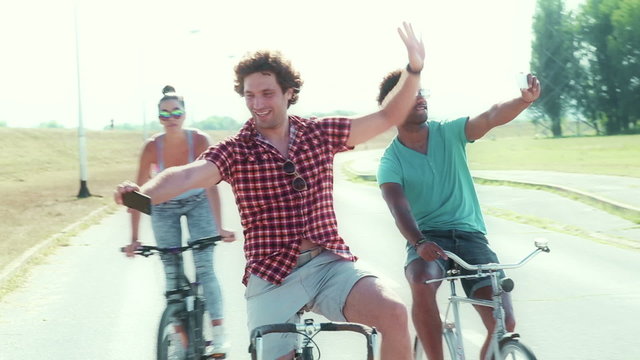 Slow motion of three young adults taking selfies on their bikes, graded