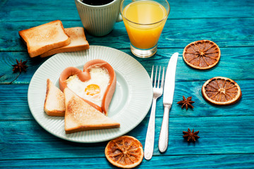 
romantic breakfast , heart-shaped fried eggs with sausage with toast, jam , hot black coffee , orange juice and spices on a wooden background