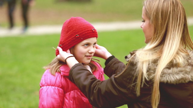 Mom putting cap on daughter's head and kissing her in forehead