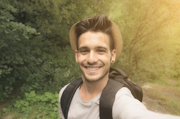 Handsome guy is taking a selfie with his smartphone in the nature - people, technology and lifestle...
