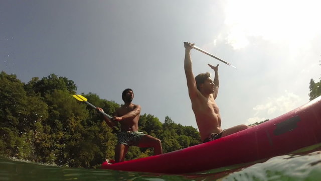 Two male friends having fun waving with paddles in a canoe