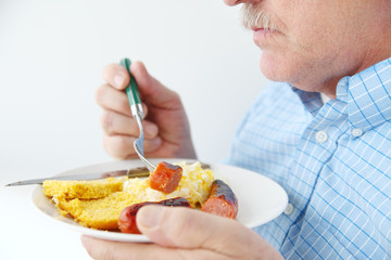 A man eating sausage, scrambled eggs and cornbread for breakfast