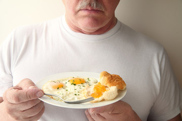 A man with a breakfast of fried eggs and a biscuit with apricot jam