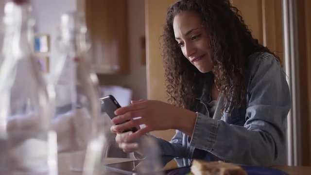 Lovely young hispanic woman in a kitchen texting on a cell phone