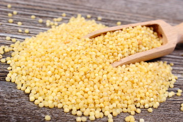 Heap of millet groats with spoon on wooden background