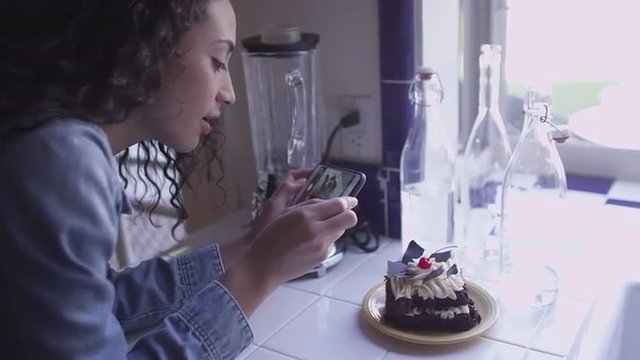 A beautiful young brunette taking pictures of cake