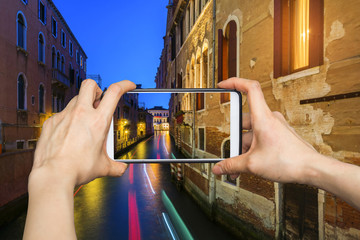 Girl taking pictures on mobile smart phone in Venice, at dusk wa