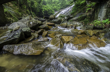 beautiful tropical river surrounded by green forest. clear water and waves. wet stone and waterfall behind