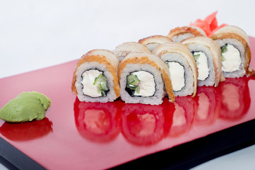 Philadelphia roll of cheese and cucumber inside wrapped in eel on a red plate with reflection on a white background