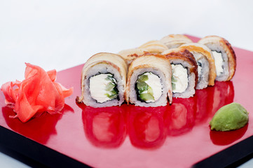 Philadelphia roll of cheese and cucumber inside wrapped in eel on a red plate with reflection on a white background