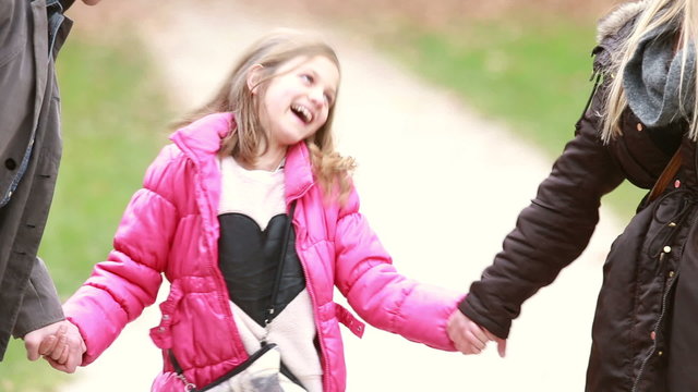 Cute little girl holding hands with parents and laughing