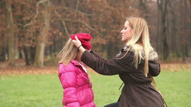 Mother putting cap on daughter's head and kissing her in forehead