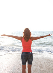 Young woman stand on beach with arms open to the sea looking at sun.